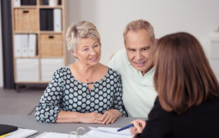 middle aged couple listening to business woman at desk