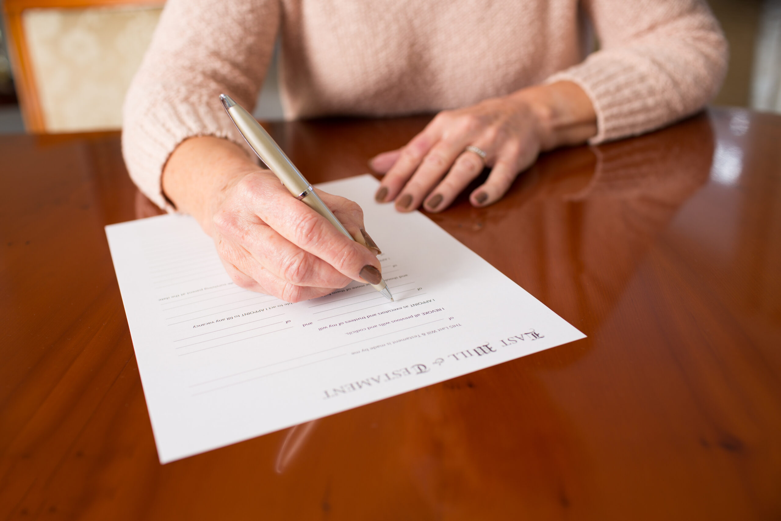 Senior Woman Signing Last Will And Testament At Home senior woman sitting at a table her writing a will