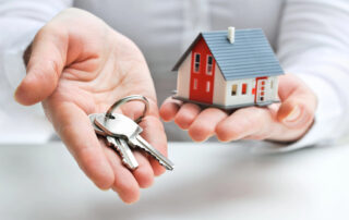 man holding miniature house in left hand and a set of keys in his right hand